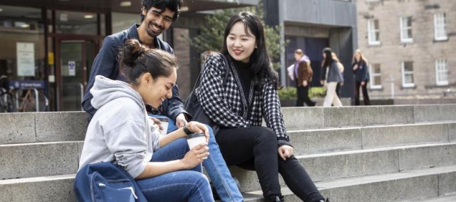 Three students sit outside the library