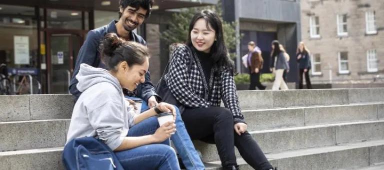 Three students sit outside the library