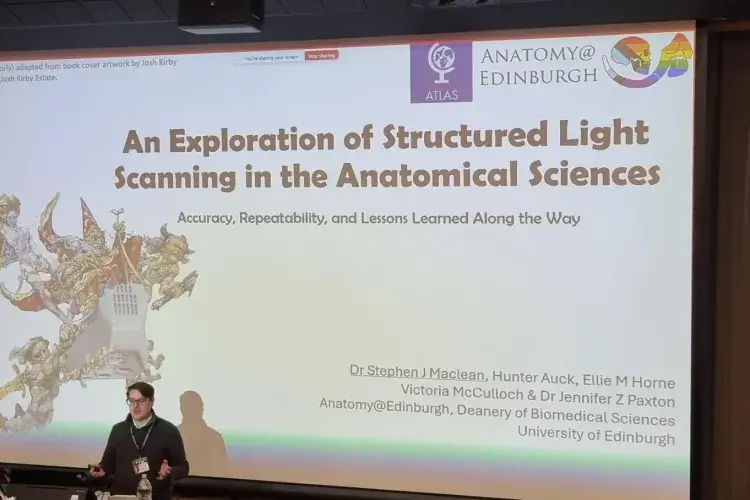 Dr Stephen Maclean standing in front of a large screen presenting his research
