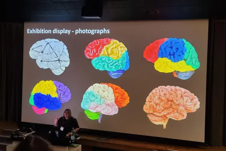 Dr Jennifer Paxton stands in front of a large screen with colourful painted brains on the screen