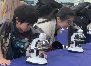Two children looking down microscopes as part of the Science festival exhibit
